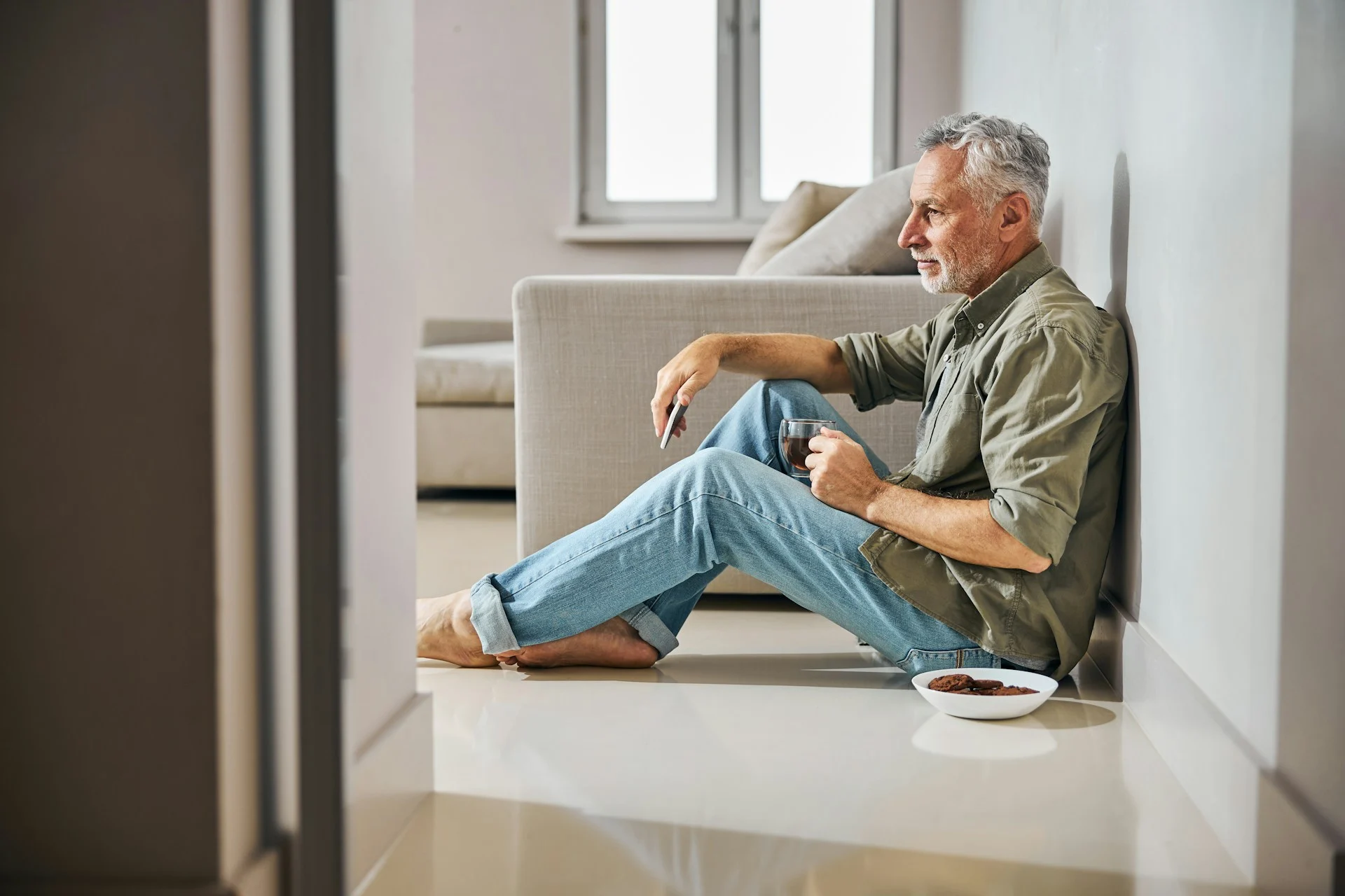 A man sitting alone by a window with a cup of coffee, thinking